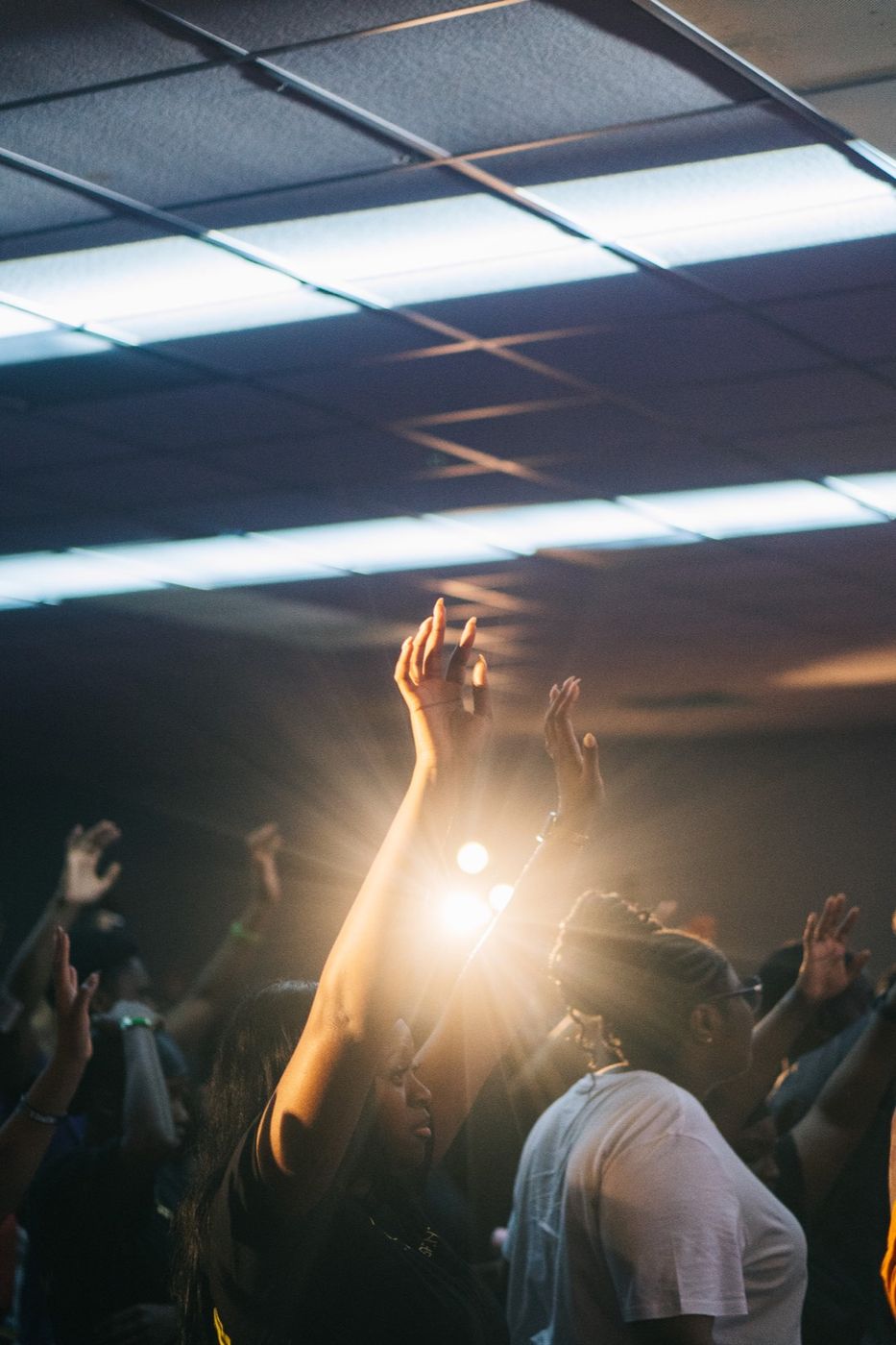 Hands raised in worship as light breaks across the room